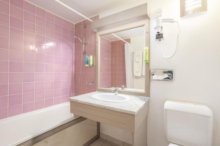 Baño completo con bañera, ducha y azulejos rosas del Karibea Squash Hôtel