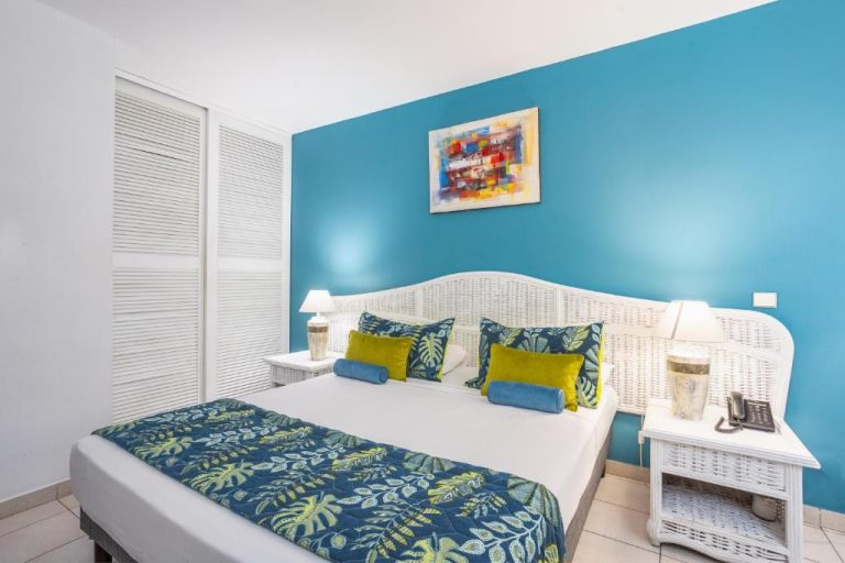 Habitación doble con pared azul turquesa y cama king size en el Karibea Squash Hôtel