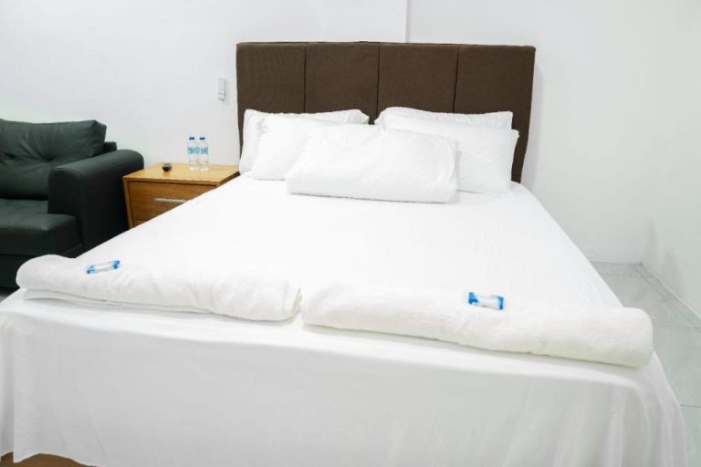 Habitación doble con cama matrimonial y toallas en Hotel Bimini, decoración en blanco y cabecero marrón
