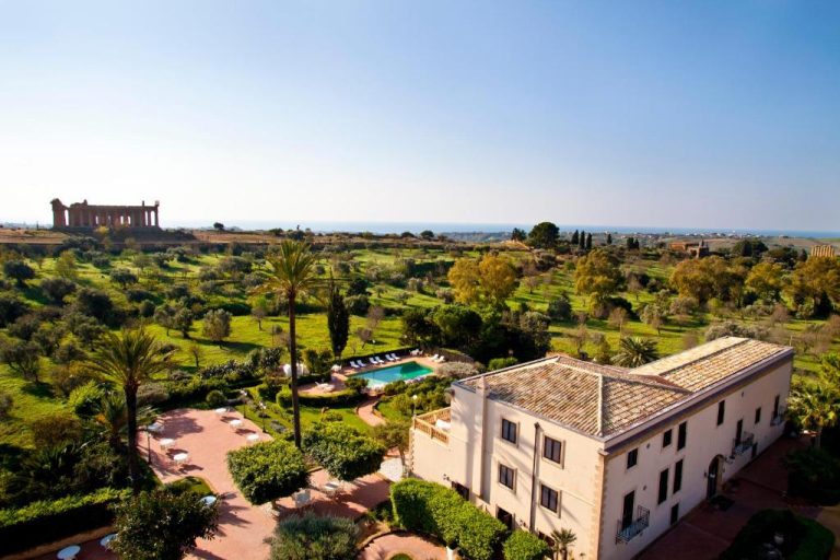 Vista aérea de la piscina exterior y jardines del Villa Athena Resort con el Templo de Agrigento al fondo