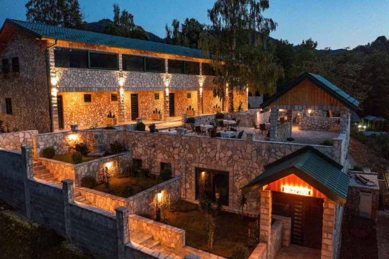 Fachada exterior de piedra iluminada del Garni Hotel Elite Resort al anochecer con terraza y jardines