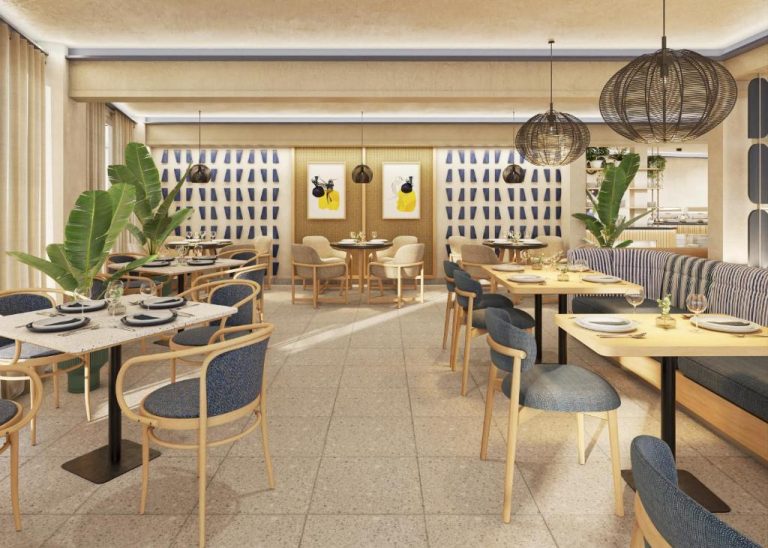 Restaurante interior del Voco Surfside Aruba con mesas de madera, sillas azules y decoración tropical mediterránea