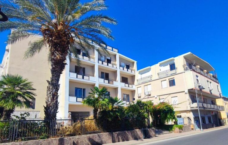 Fachada exterior del Hotel Corallo New con palmeras y balcones bajo un cielo azul mediterráneo