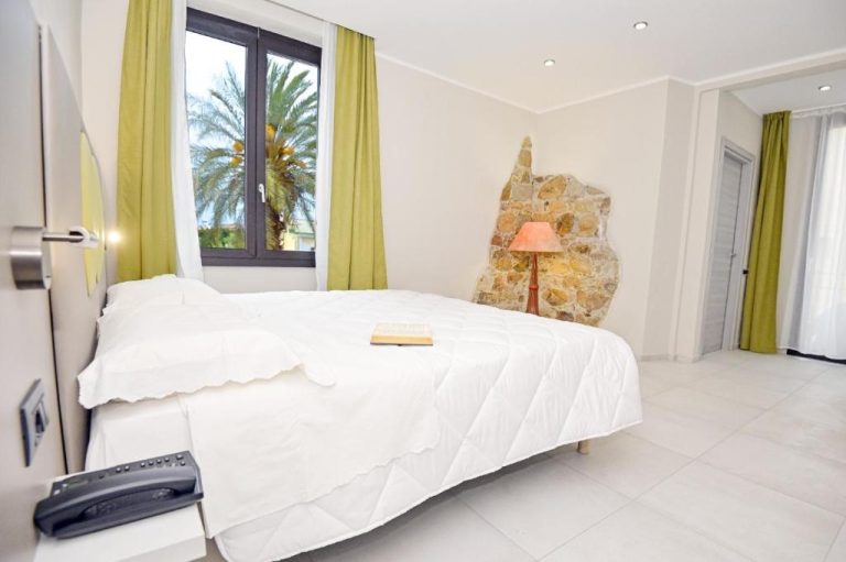Habitación doble con cama blanca y pared de piedra natural en Hotel Corallo New