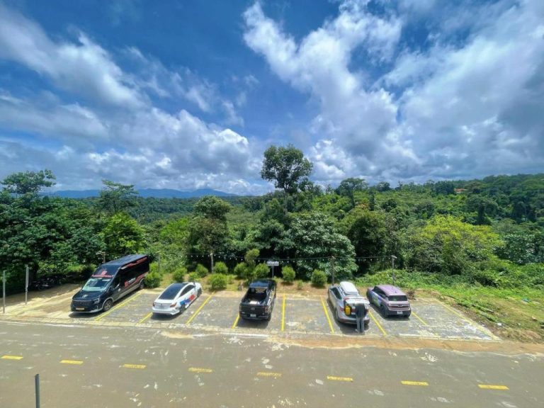 Aparcamiento exterior del MăngDiang Boutique Hotel rodeado de exuberante vegetación y montañas al fondo