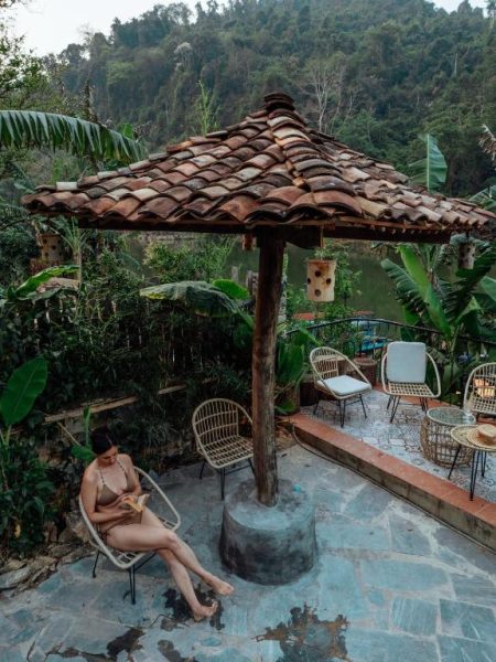 Terraza exterior con sombrilla rústica y sillas de ratán rodeada de selva tropical en Ba Be Jungle Houses