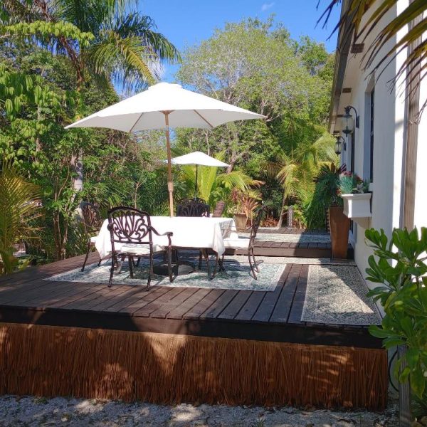 Terraza de madera con mesas y sombrillas blancas rodeada de vegetación tropical en The Pilot House