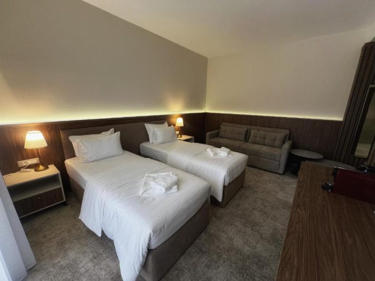 Habitación twin con dos camas individuales y sofá en el Hotel Onogošt, decoración moderna en tonos madera