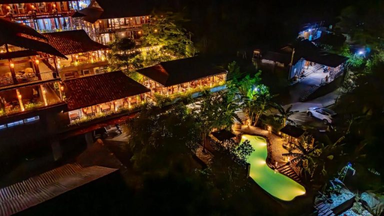 Vista aérea nocturna de la piscina iluminada y bungalows tropicales del Ba Be Jungle Houses