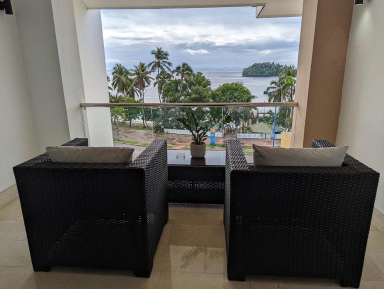 Balcón con sillones de ratán y vista panorámica al mar y palmeras en Hacienda Samana Bay Hotel