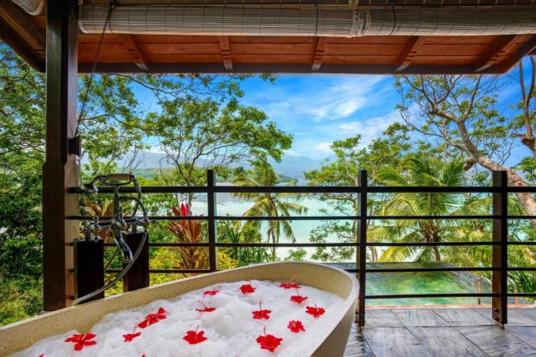 Bañera de hidromasaje con flores rojas en terraza exterior del Enchanted Island Resort con vistas al mar