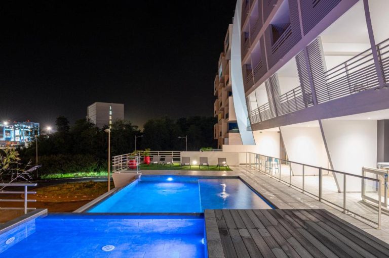 Piscina exterior iluminada de noche en B&B Home Fort-de-France Marina con terraza y edificio moderno