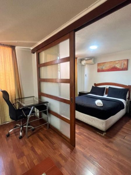 Habitación con cama doble y escritorio de vidrio separados por puerta corrediza en Dptos Merced Santiago