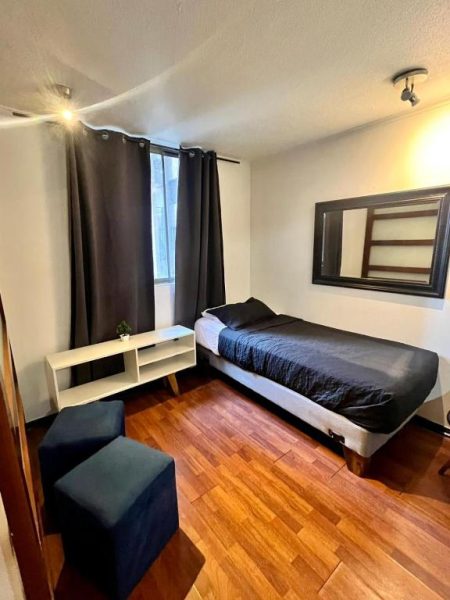 Habitación individual con cama, piso de madera y cortinas negras en Dptos Merced Santiago