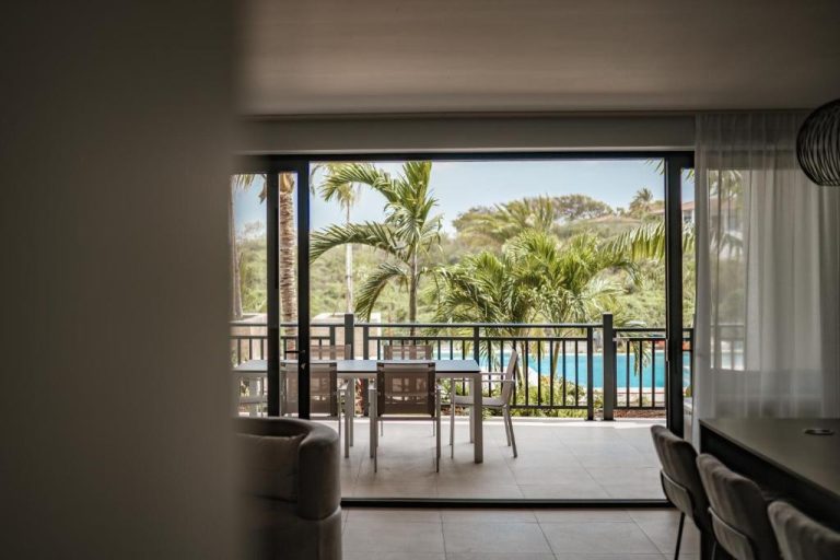 Balcón con mesa y sillas del The Breeze Blue Bay Curaçao con vistas a la piscina y palmeras tropicales