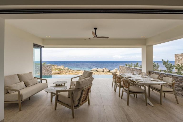 Terraza cubierta con sala y comedor exterior con vistas al mar en The Ridge Blue Bay Curaçao Resort