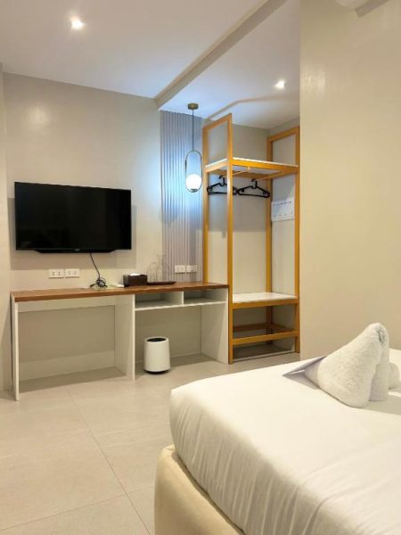 Habitación doble moderna con televisión, escritorio y armario abierto en Olive's Suites