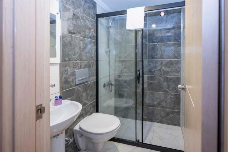 Baño moderno con ducha de cristal y revestimiento de mármol gris en Legend Tulip Hotel