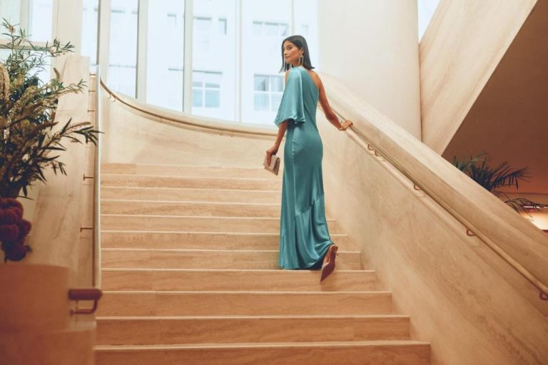 Mujer con vestido de gala subiendo la elegante escalera de mármol del Regent Santa Monica Beach by IHG