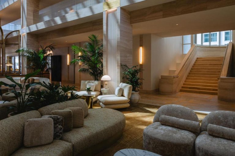 Elegante lobby del Regent Santa Monica Beach con sofás, plantas tropicales y escalera de mármol
