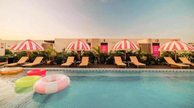 Piscina exterior con flotadores, tumbonas y sombrillas de rayas en Privada Stays Boutique Hotel