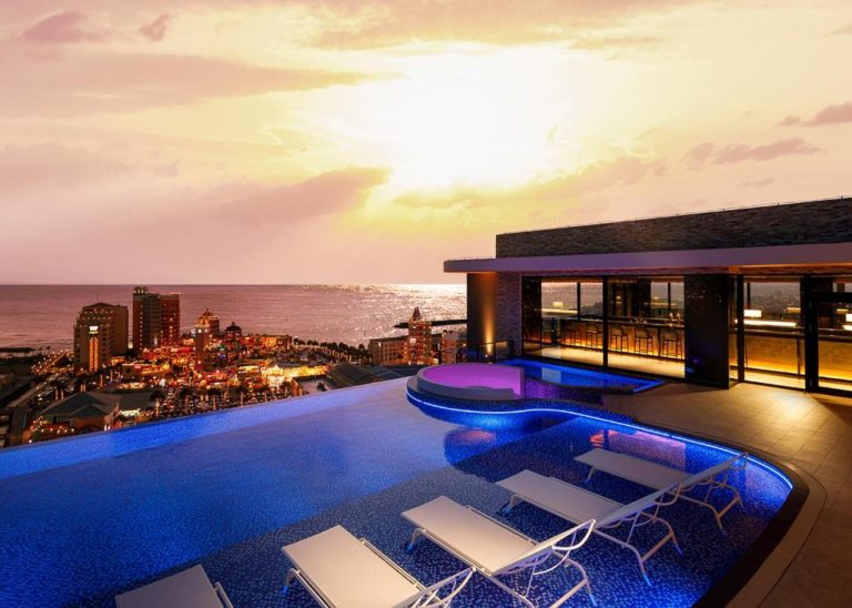 Piscina infinita con jacuzzi iluminado y vistas al océano al atardecer en RIHGA Royal Resort Okinawa Chatan