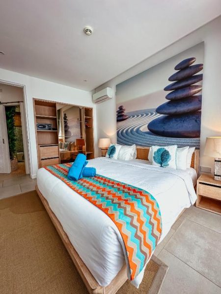 Suite con cama king size y decoración zen en AQUA Boutique Hotel, colcha de colores y mural de piedras