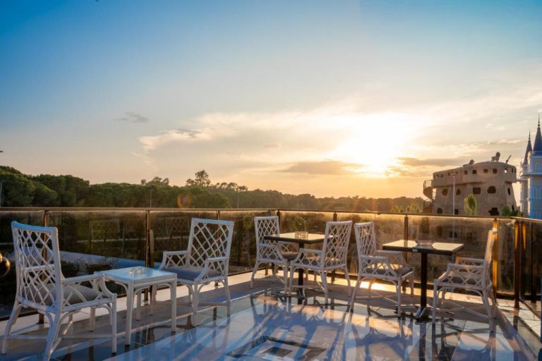 Terraza con sillas y mesas blancas del Velaris Boutique Hotel con vistas al atardecer y jardines