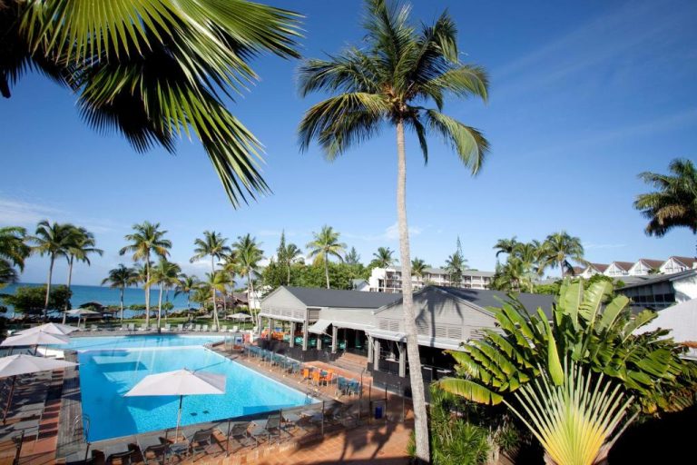 Piscina exterior rodeada de palmeras tropicales con vista al mar en La Creole Beach Hotel & Spa