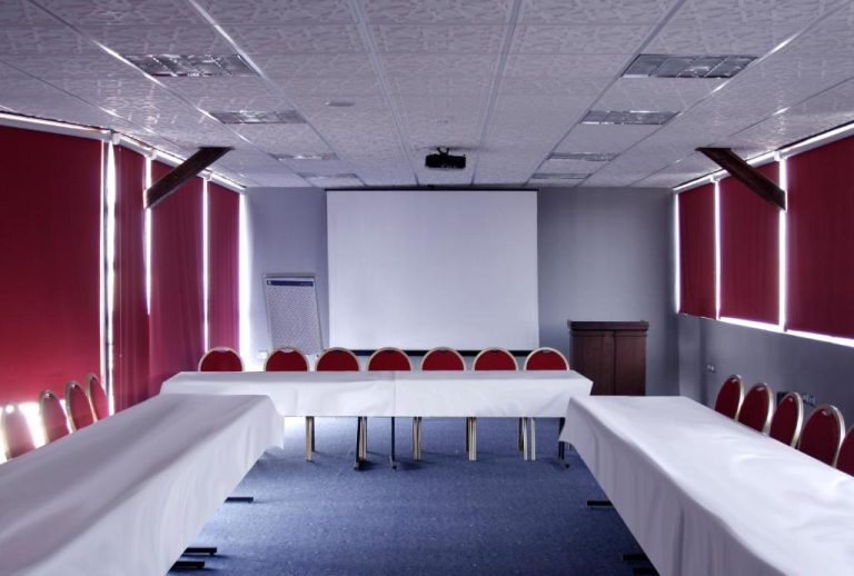Sala de conferencias con mesas en U, sillas rojas y pantalla de proyección en Mariam Hotel