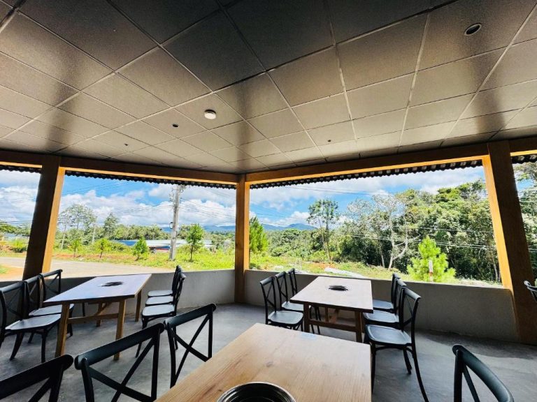 Terraza restaurante con mesas y sillas negras y vistas al bosque y montañas en Chimney Hotel Măng Đen