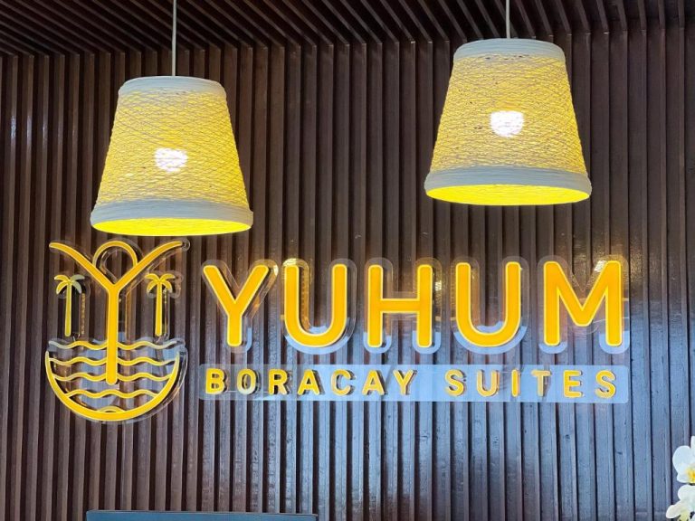 Recepción del Yuhum Boracay Suites con logo iluminado en dorado y lámparas de mimbre