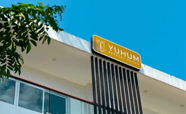 Fachada exterior del Yuhum Boracay Suites con cartel identificativo y cielo azul