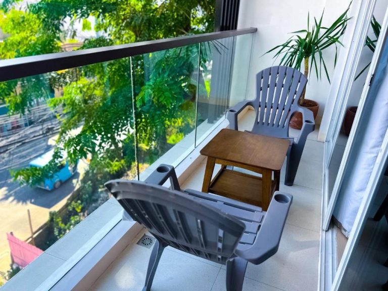 Terraza con sillas y mesa de madera en Yuhum Boracay Suites con vistas a la calle y vegetación