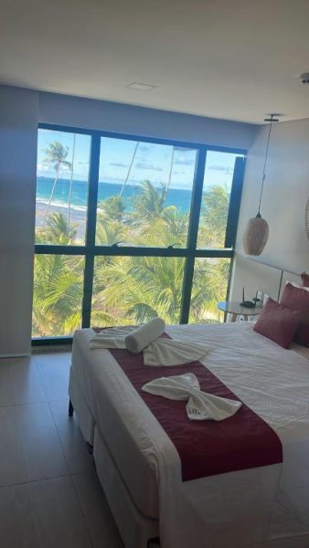 Habitación con cama doble y vista panorámica al mar y palmeras en Porto Beach Resort Marulhos Prime