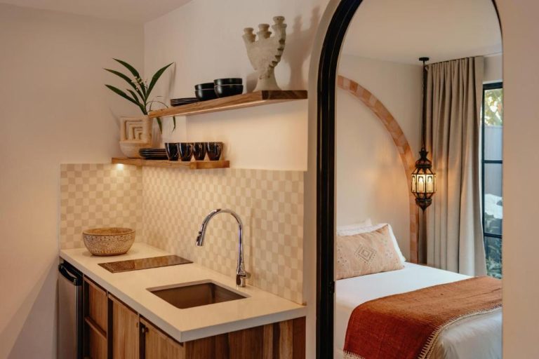 Kitchenette con fregadero y estantes de madera junto a dormitorio con arco en Domo Nosara Boutique Hotel