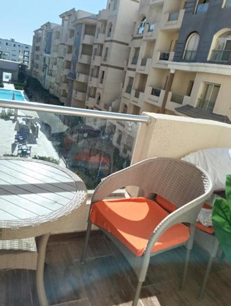 Balcón con sillas de ratán y cojines naranjas con vistas a la piscina del Resort Florenza