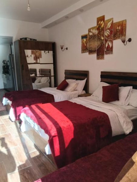 Habitación triple con camas en tonos rojos y blancos en el Resort Florenza, decoración elegante con armario de madera