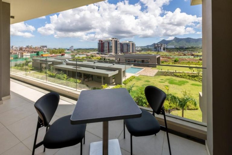 Terraza con mesa y sillas del Minissy Suites con vistas a la piscina, jardines y ciudad al fondo