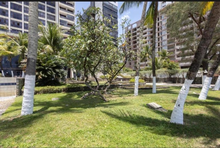 Jardines tropicales con palmeras y césped del Hotel Golden Beach Flat con edificios al fondo
