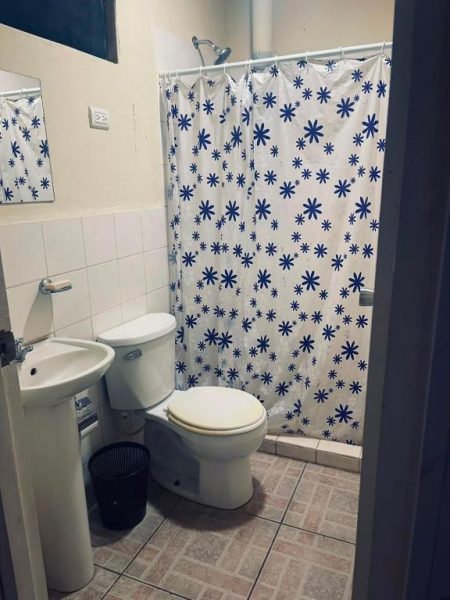 Baño privado con ducha, inodoro y lavabo del Hostal Pequeña Habana con cortina decorativa azul