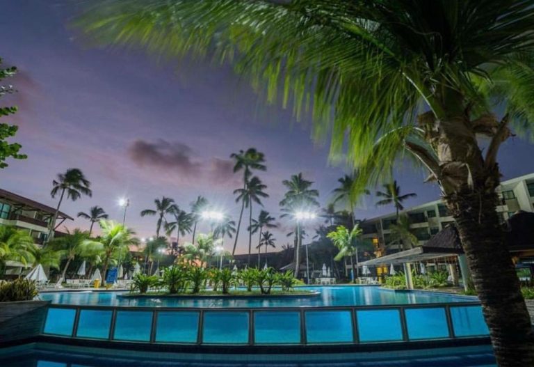 Piscina iluminada de noche con palmeras tropicales en Porto Beach Resort Marulhos Prime, Brasil