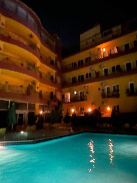 Piscina exterior iluminada de noche con vistas a la fachada del Mariam Hotel