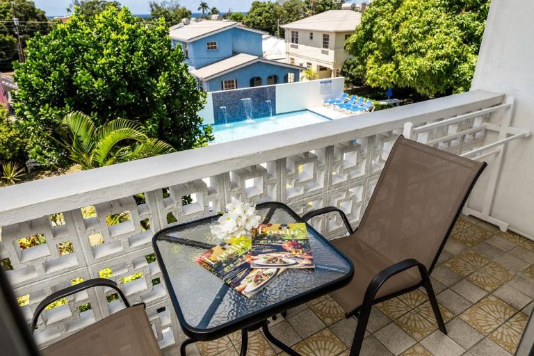 Balcón con mesa y sillas de Adulo Apartments con vistas a la piscina exterior y jardines tropicales