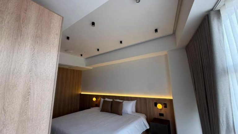 Habitación doble moderna con iluminación cálida y cabecero de madera en Autenthico Atempo Local Suites Medellín