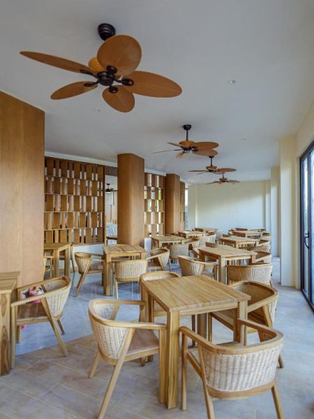 Restaurante del Hotel Kinan Sentral con mesas de madera, sillas de ratán y ventiladores tropicales en el techo