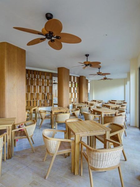Restaurante del Hotel Kinan Sentral con mesas de madera, sillas de ratán y ventiladores de techo tropicales