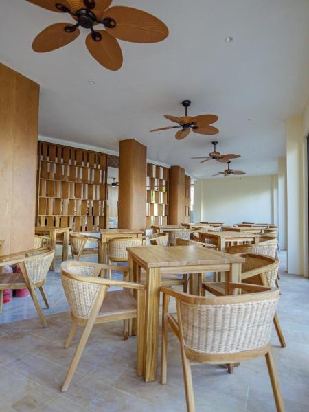 Restaurante del Hotel Kinan Sentral con mesas de madera, sillas de ratán y ventiladores de techo tropicales