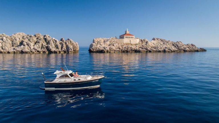 Vista desde barco al faro del Palace Natali en isla rocosa rodeada de aguas cristalinas del Adriático