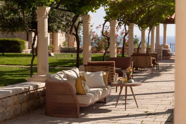 Terraza exterior con sofás y columnas del Palace Natali rodeada de jardines con vistas al mar